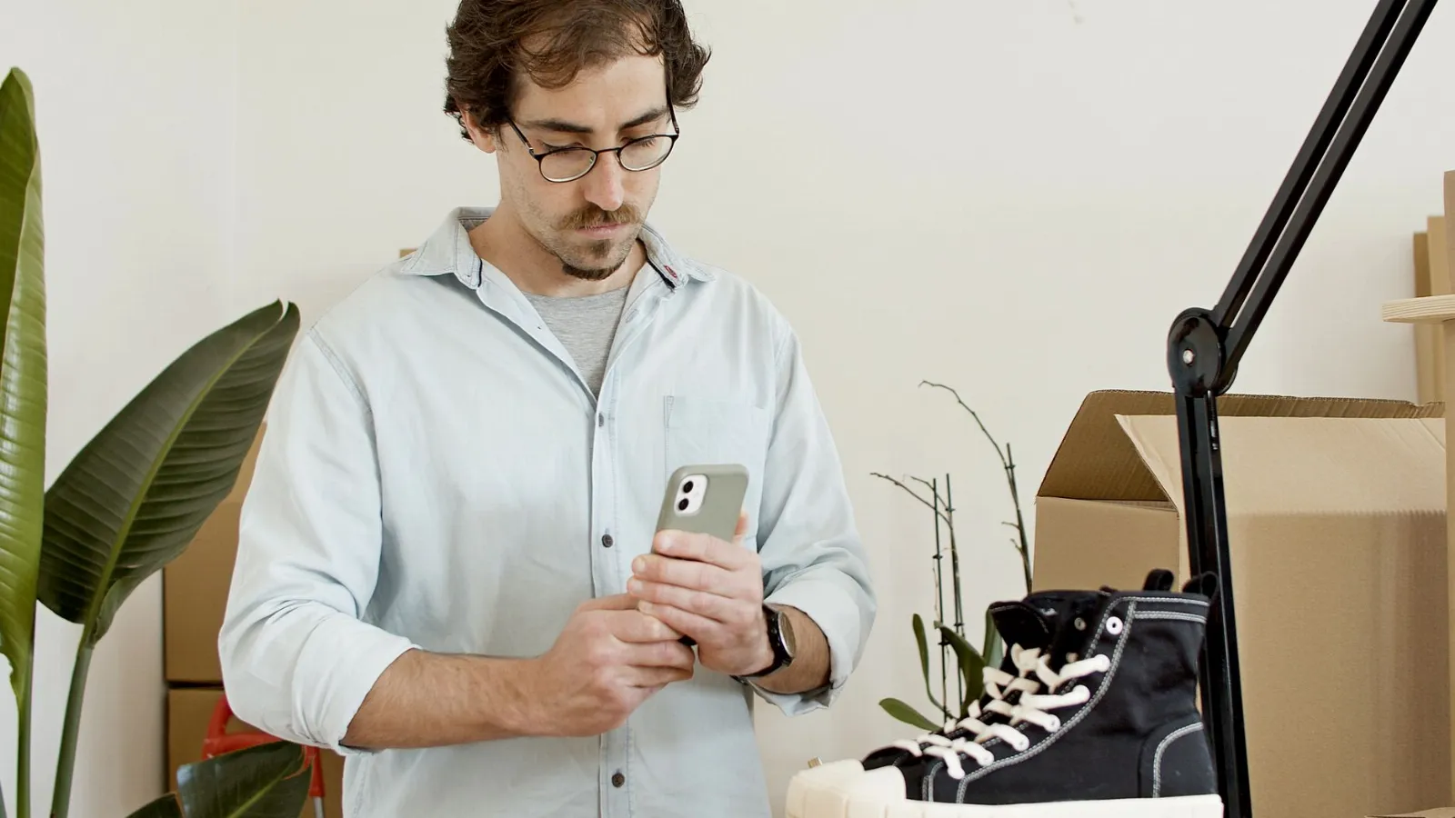 Vendedor revisando fotos en su celular junto a zapatos y cajas para compartir su catálogo en el Estado de WhatsApp