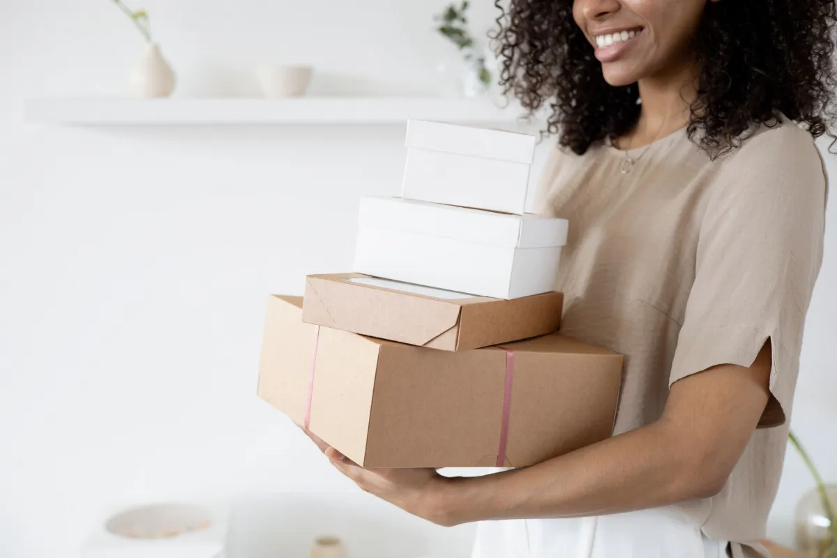 Mujer sonriente sostiene cajas de productos, ejemplo de cuántos productos poner en un catálogo de WhatsApp